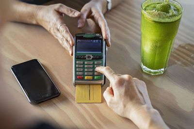 Cropped hands of female customer making credit card payment to owner on wooden table in cafeteria