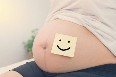 Midsection of pregnant woman with anthropomorphic smiley face on belly