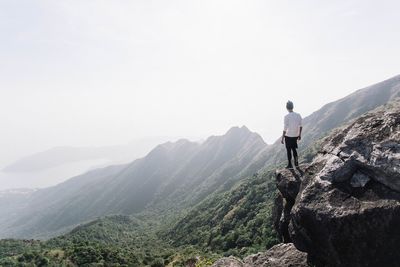 Full length rear view of man standing cliff against sky