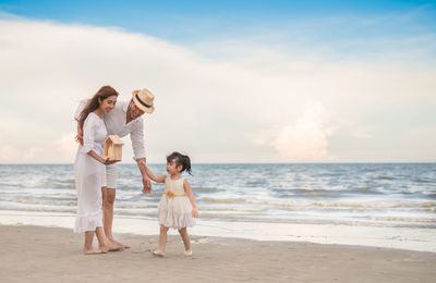 Full length of couple with daughter at beach against sky