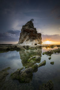 Rock formation in sea against sky during sunset