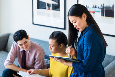 Businesswoman using graphics tablet while coworkers discussing over documents in office