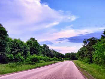 Empty road along plants and trees against sky