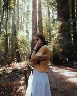 Woman standing by tree trunks in forest