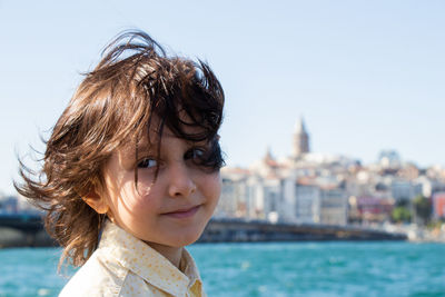 Smiling boy standing by river against buildings