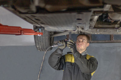 Young mechanic man working hard under the car in workshop garage