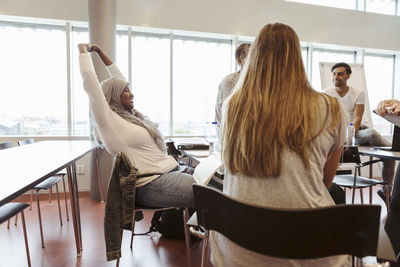 Smiling bored woman with arms raised looking at friends in classroom