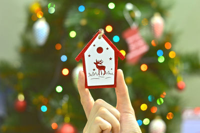 Cropped hand holding decoration against illuminated christmas tree