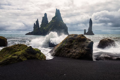 Sea waves splashing on rocks against sky