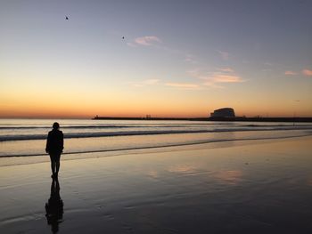 Silhouette man standing on beach against sky during sunset