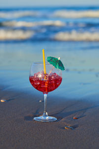 Close-up of wineglass on glass against the beach