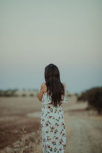 Rear view of woman standing on field against clear sky