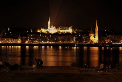 View of illuminated buildings by river at night