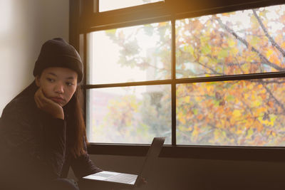 Young woman looking through window while sitting on table