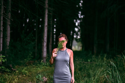 Woman holding leaves over face while standing on grass in forest