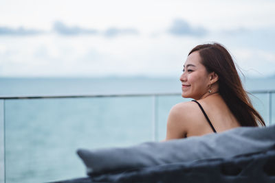 Portrait of young woman looking at sea against sky