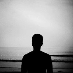 Rear view of silhouette man standing by sea against clear sky