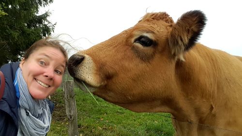 Portrait of smiling mature woman standing by cow against sky