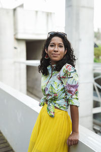 Smiling young woman in colorful dress leaning on retaining wall