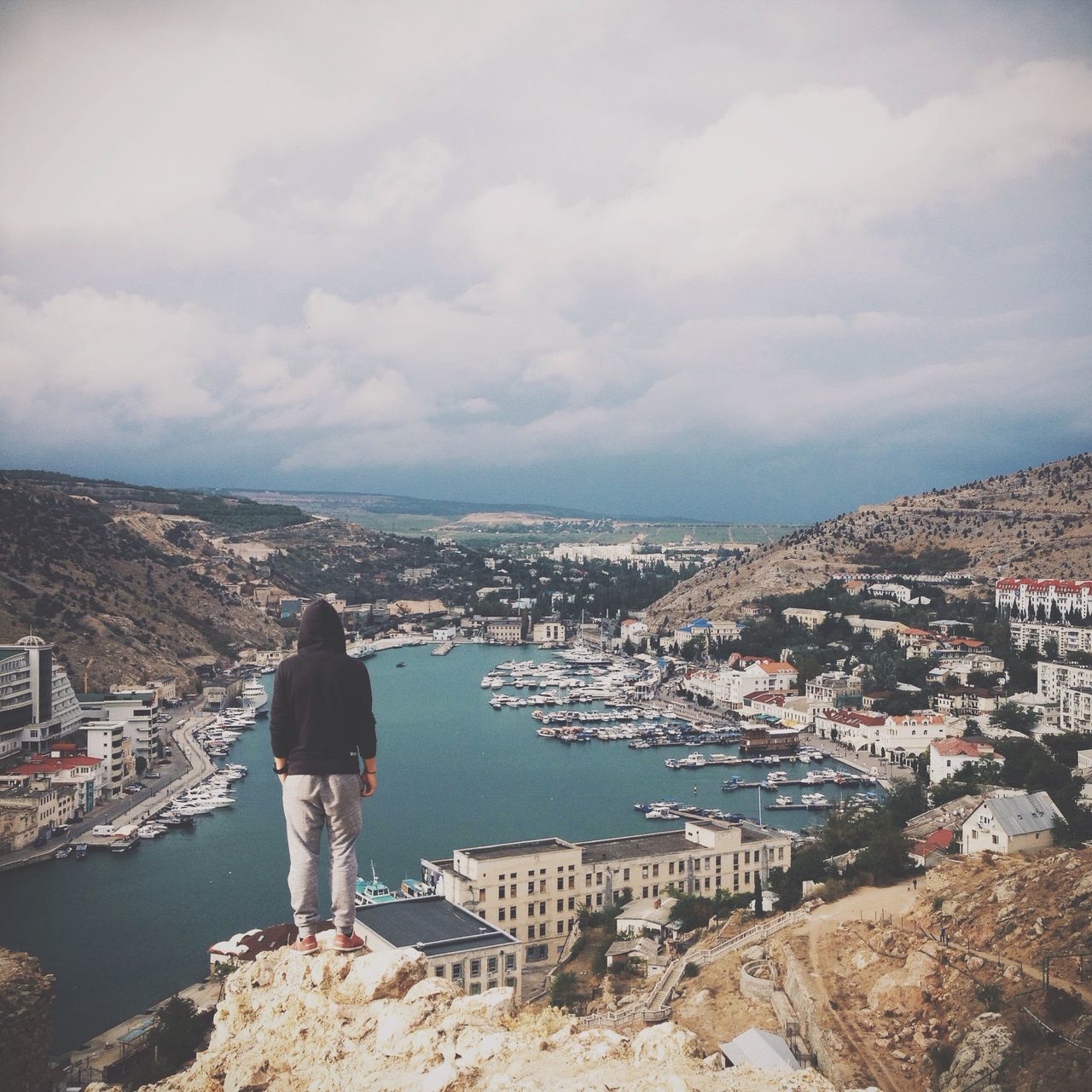 water, building exterior, architecture, built structure, sky, rear view, lifestyles, men, cloud - sky, leisure activity, standing, casual clothing, sea, person, city, rock - object, cityscape, full length