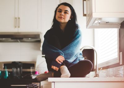 Portrait of young woman sitting on kitchen counter at home