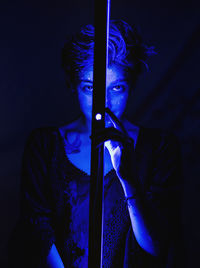 Portrait of young woman holding illuminated purple light in darkroom