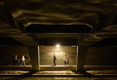 People walking on illuminated bridge at night