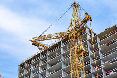 Low angle view of crane at construction site against sky