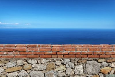 Stone wall by sea against blue sky