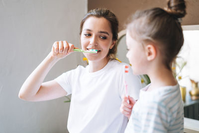 Young mother woman with little tween girl daughter in pajamas brushing their teeth at home