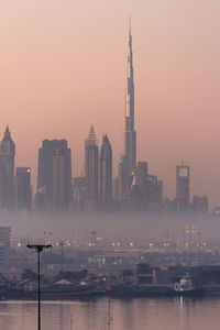 Harbor by cityscape at dawn against sky