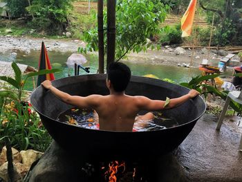 Rear view of shirtless boy sitting in water