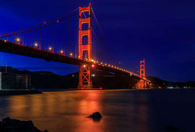 Illuminated bridge over river against sky at night