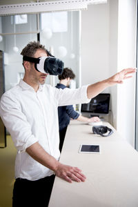 Businessman examining virtual reality simulator while coworker using computer in office