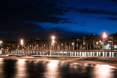 Illuminated buildings by river against sky at night