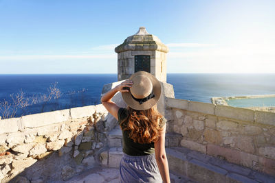 Traveler girl walking towards watchtower on santa barbara castle in alicante city, spain