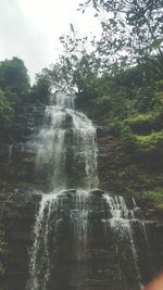 Waterfall in forest against sky