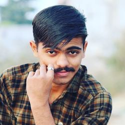 Close-up portrait of young man holding mustache outdoors