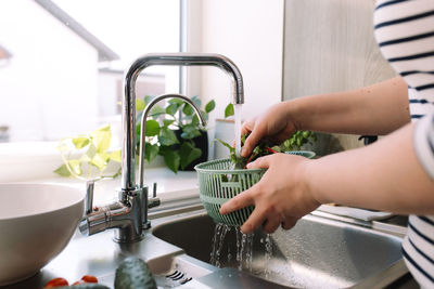 Woman washing green salad leaves for salad in kitchen in sink under running water