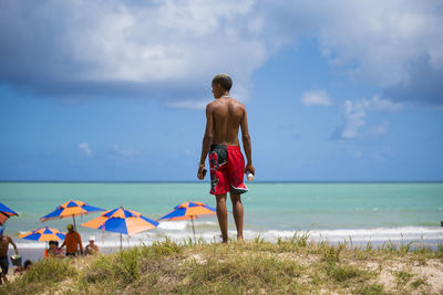 Rear view of shirtless man standing on beach