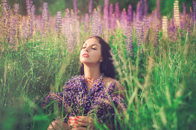 Beautiful young woman standing by purple flowers on field