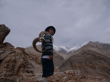 Man standing with animal skull on rock against sky