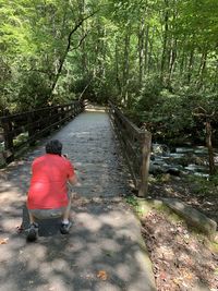 Rear view of woman sitting on sidewalk in forest