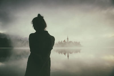 Woman in gray coat watching a sunrise among the fog on the shores of lake bled, slovenia iii