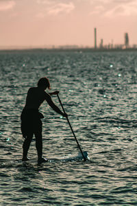 Silhouette man standing in sea against sky during sunset