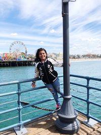 Portrait of young woman standing by railing against sky