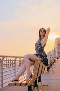 Portrait of young woman sitting on seat against sky during sunset