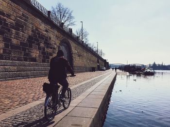 Rear view of man riding bicycle on street by canal