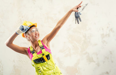 Female worker in coverall pointing while standing against wall