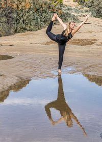 Reflection of woman practicing yoga in water at beach